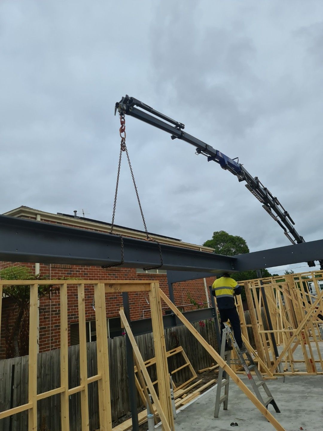 A man is standing on a ladder while a crane is lifting a beam.