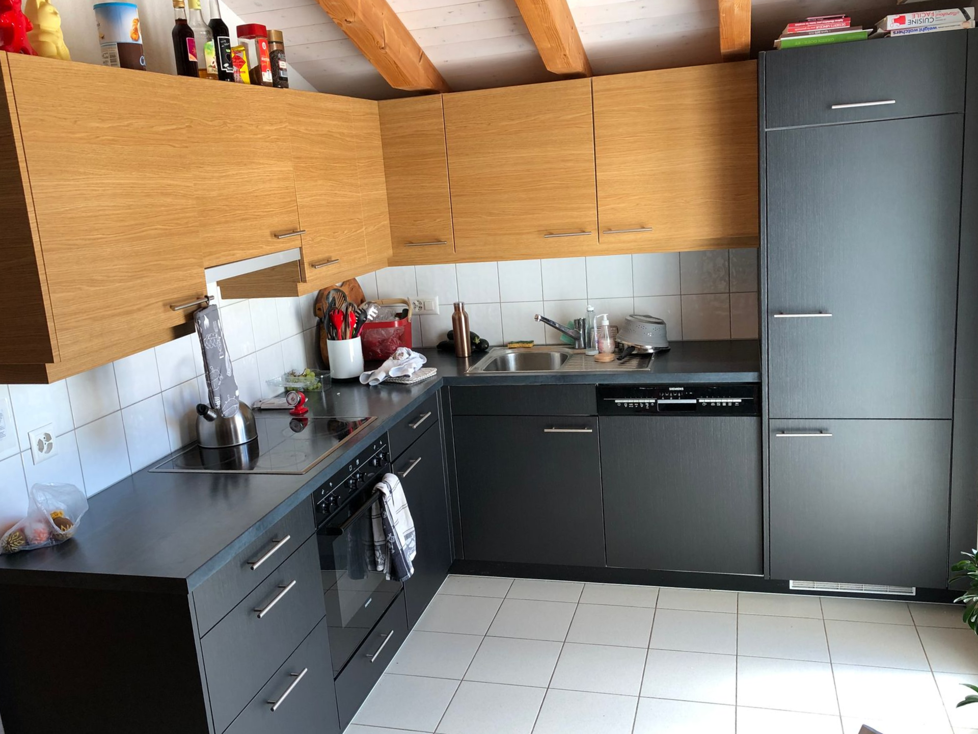 Cuisine moderne avec armoires grises, armoires hautes en bois, sol carrelé et électroménagers en acier inoxydable