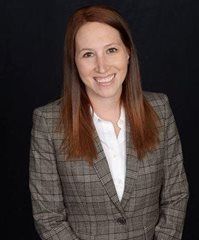 Woman in a plaid blazer and white shirt smiles, against a black background.