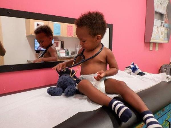 Child with stethoscope examining a stuffed animal in a doctor's office.