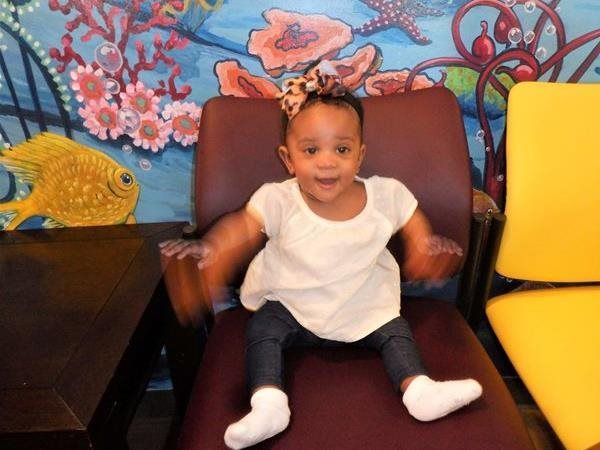 Happy toddler in white top and jeans sitting on chair, background has ocean mural.