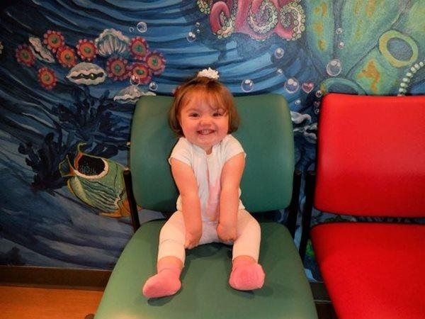 Smiling toddler sits on a green chair in front of an underwater mural.