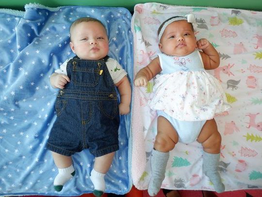 Two babies lying down on blankets; one in denim overalls, the other in a dress.