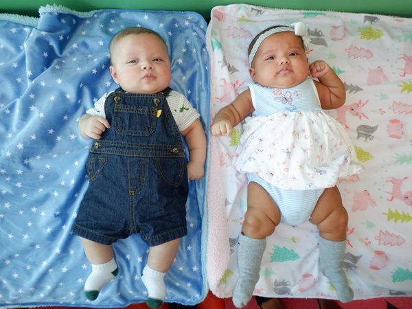 Two babies lying down on blankets; one in denim overalls, the other in a dress.