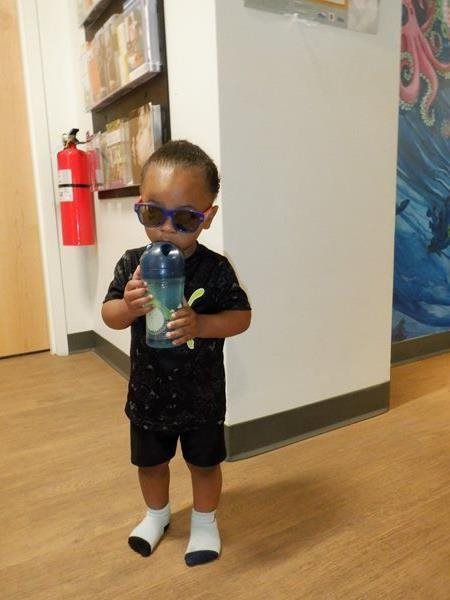 Young child wearing sunglasses and drinking from a water bottle in a library.