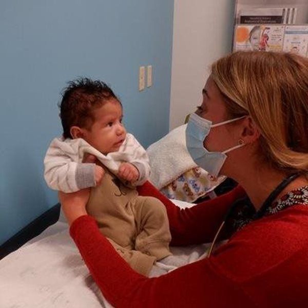 A person in a mask holds a baby during a medical examination in an office.