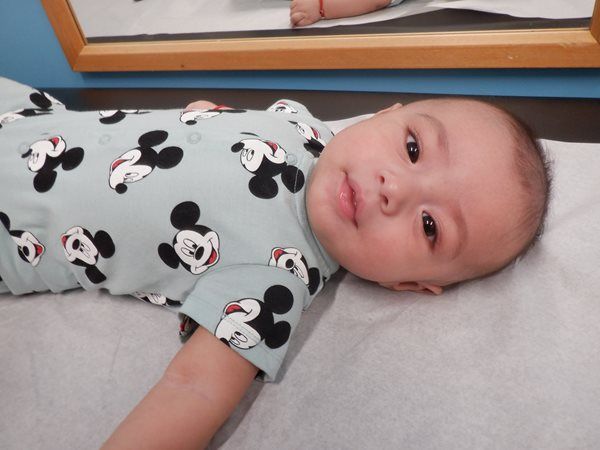 Baby in Mickey Mouse onesie lying on a white paper surface, looking at the camera.