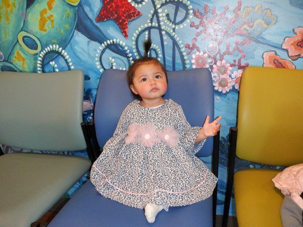 Girl in a dress sitting on a blue chair, colorful wall art in background.