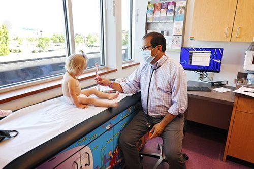 Doctor examines a child on an exam table. The child sits facing the doctor who is holding a medical instrument.