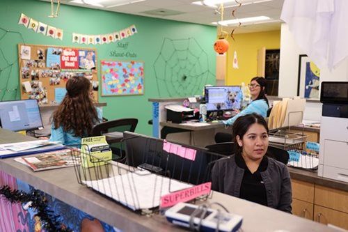 Three people working at a reception desk in an office decorated with Halloween elements.