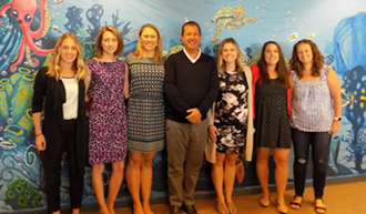 Group of people posing in front of a colorful mural featuring sea creatures.