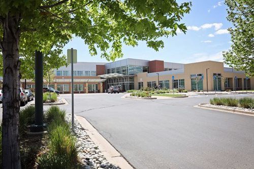 Hospital building with trees, blue sky, and a paved circular driveway.