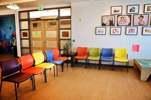 Colorful chairs in a waiting room with photos on the wall and wooden doors.