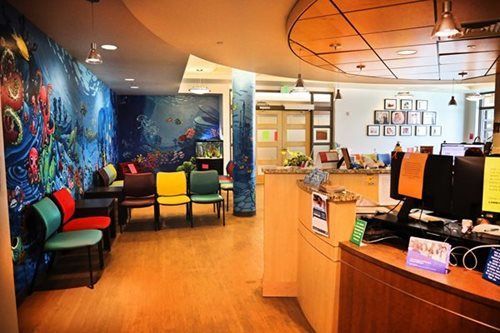 Pediatric waiting room with colorful mural, chairs, and front desk.