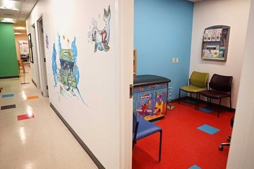 Hallway and exam room in a pediatric clinic with colorful artwork, red floor, and chairs.