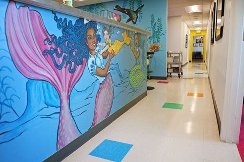 Hallway with mermaid mural, colorful floor squares, and receding row of lights.
