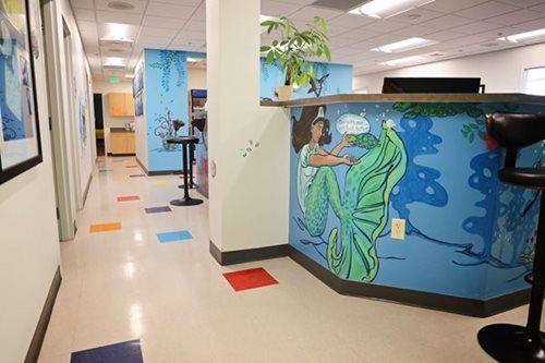 Hallway with mermaid mural, reception desk, colorful floor tiles, and artwork.