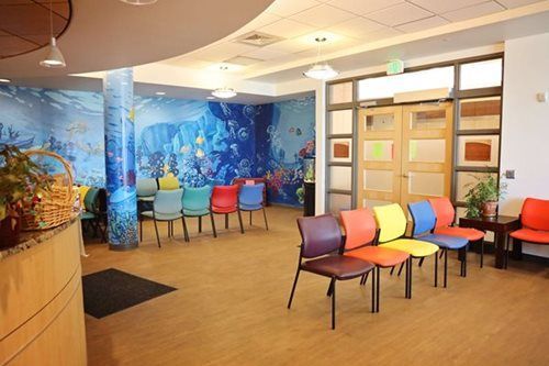 Waiting room with colorful chairs, an underwater mural, and a wooden door.