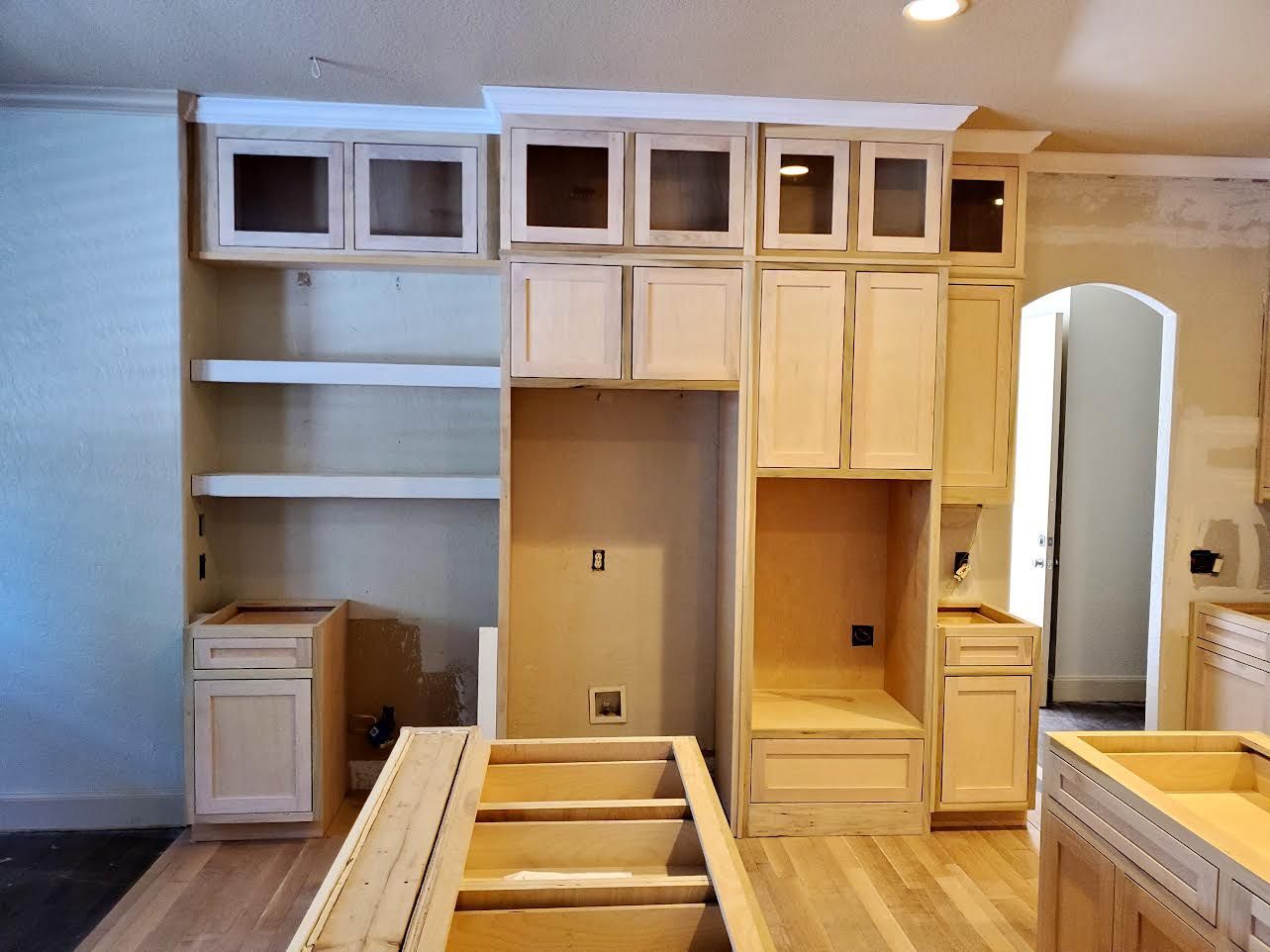 Kitchen under renovation; unfinished wood cabinets, shelving, and island; empty appliance spaces; room with hardwood floors.