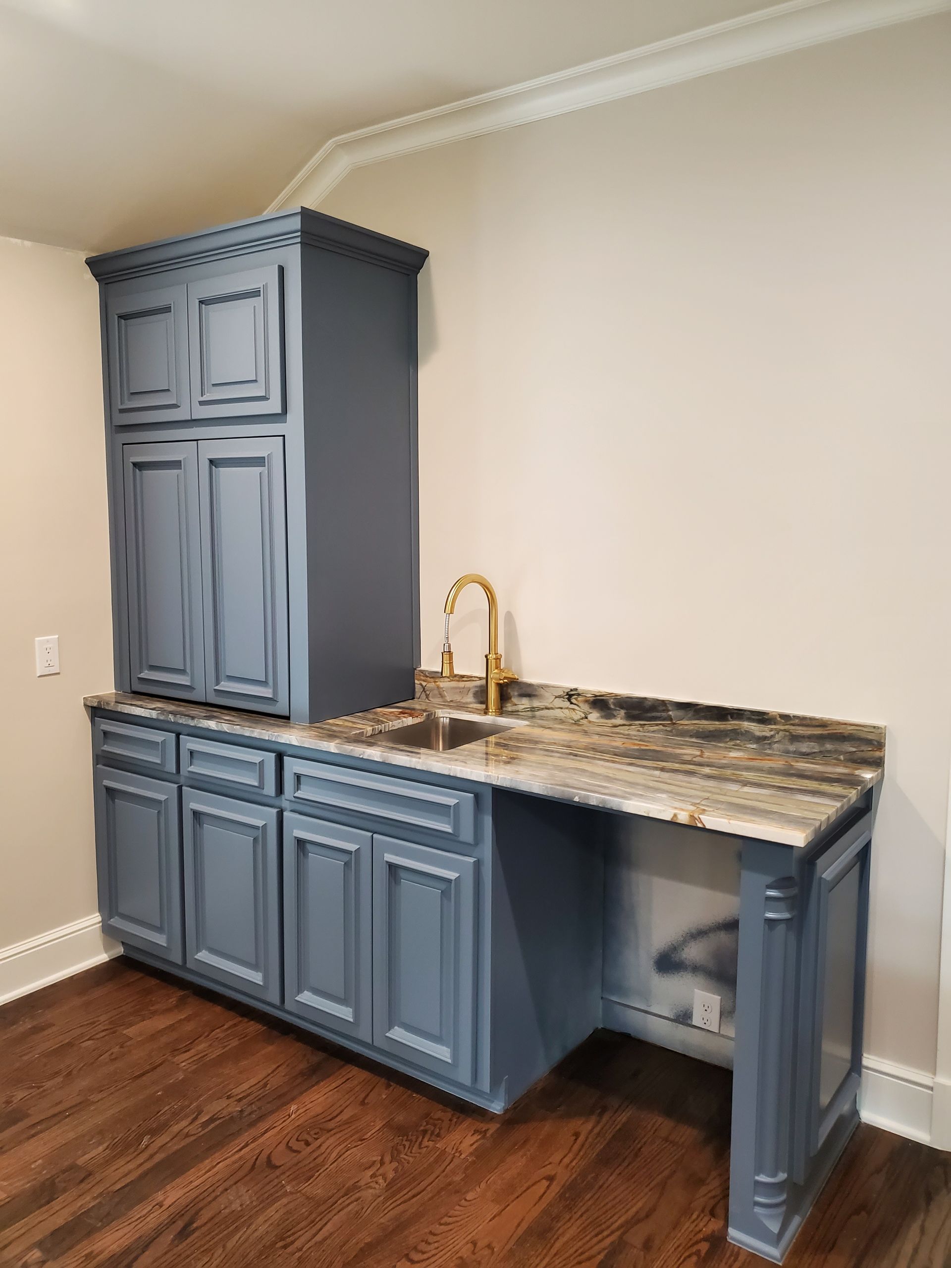 Blue cabinets with a built-in sink and countertop. A gold faucet is installed. The setting is a room with wood flooring.