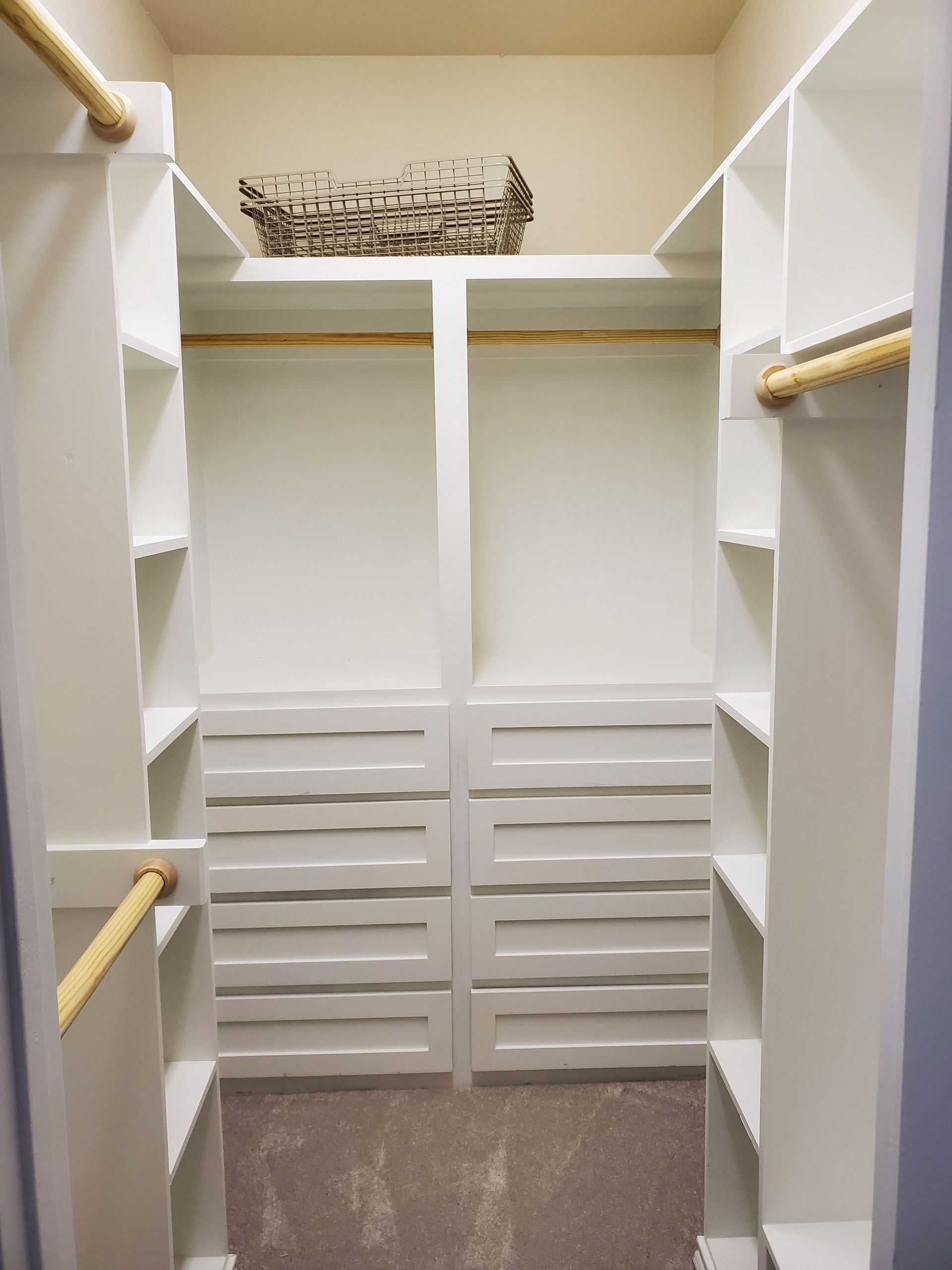 A walk-in closet with white shelves, drawers, and hanging rods. A woven basket sits on a top shelf.