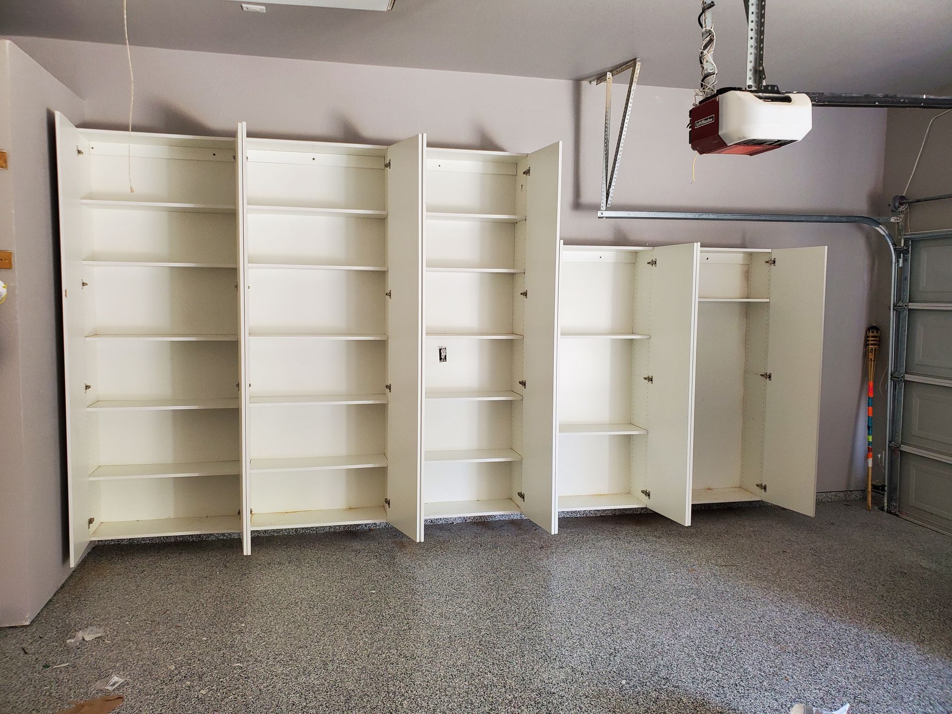 Garage with white storage cabinets mounted on a wall, with shelves visible. 