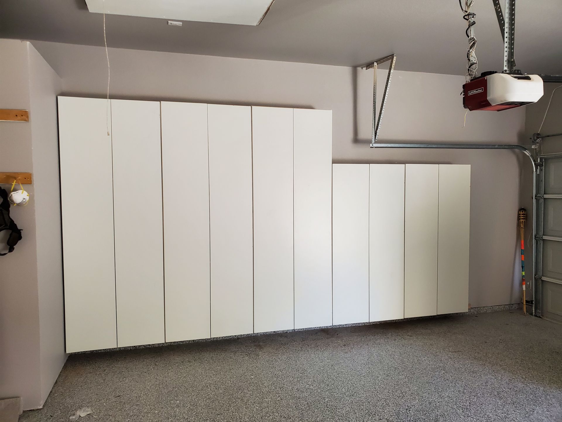 White garage cabinets installed on a gray wall. The cabinets are closed and the garage floor is gray.
