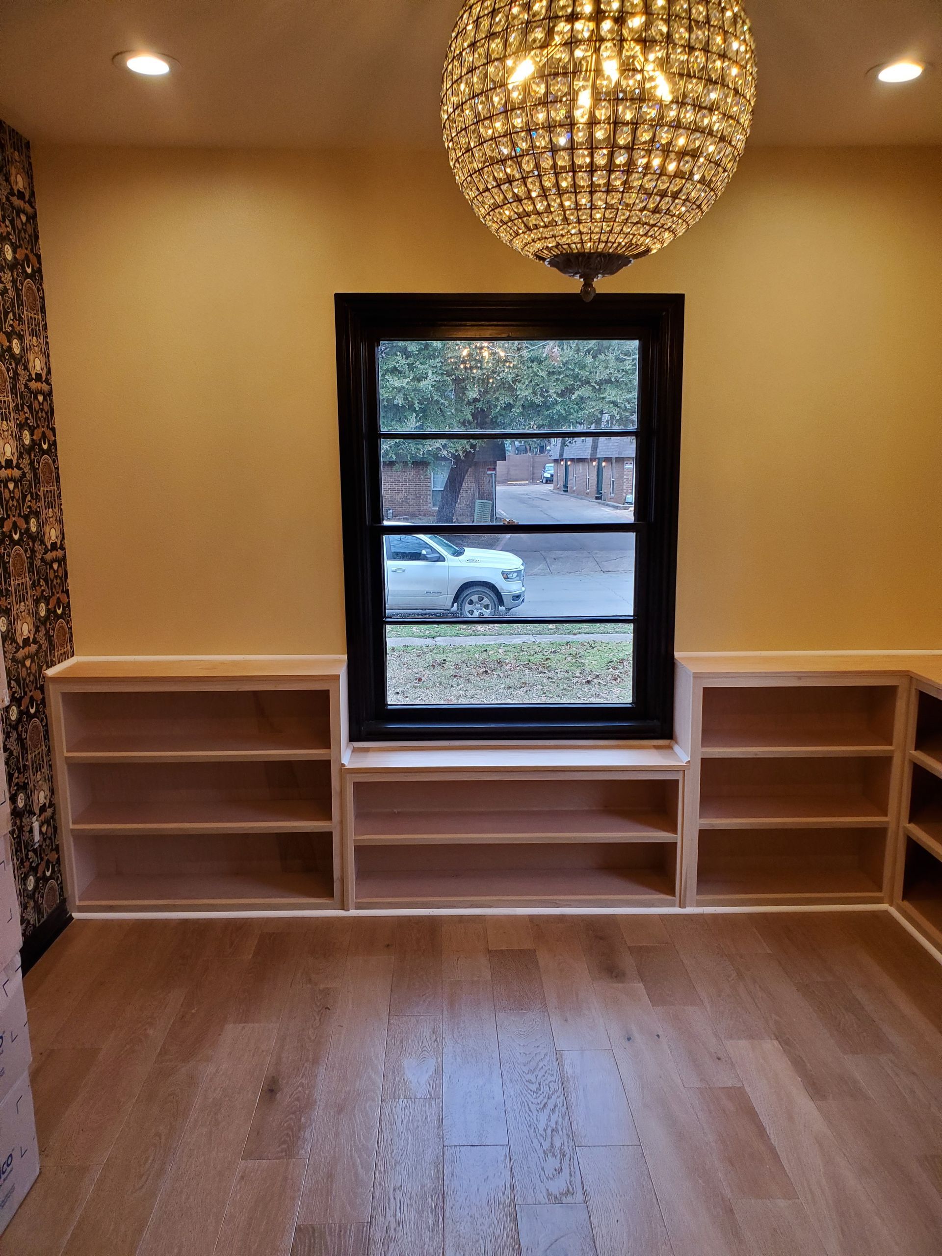 Interior room with built-in bookshelves flanking a black-framed window. A crystal chandelier hangs from the ceiling.