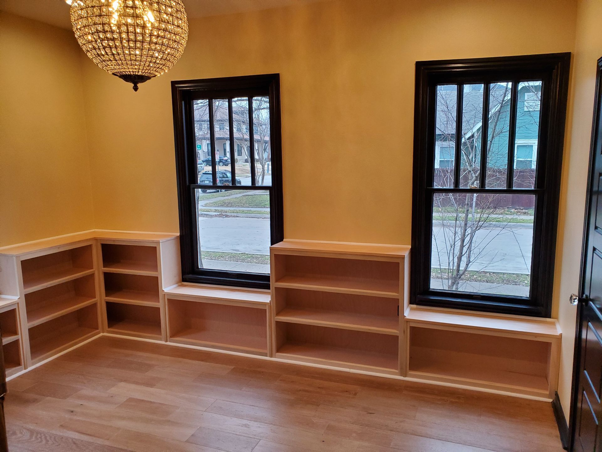 A room with two windows and built-in bookshelves. The windows have black frames, and the walls are painted yellow. 