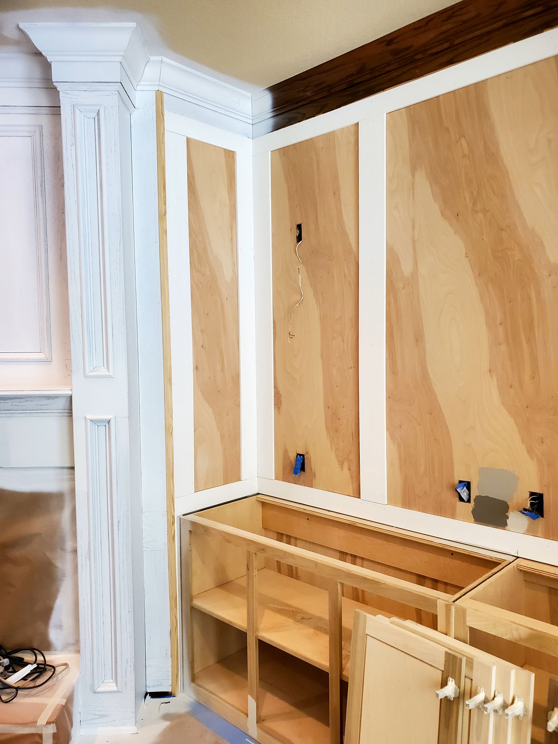 Kitchen under construction with plywood walls, white trim, and unfinished cabinets.