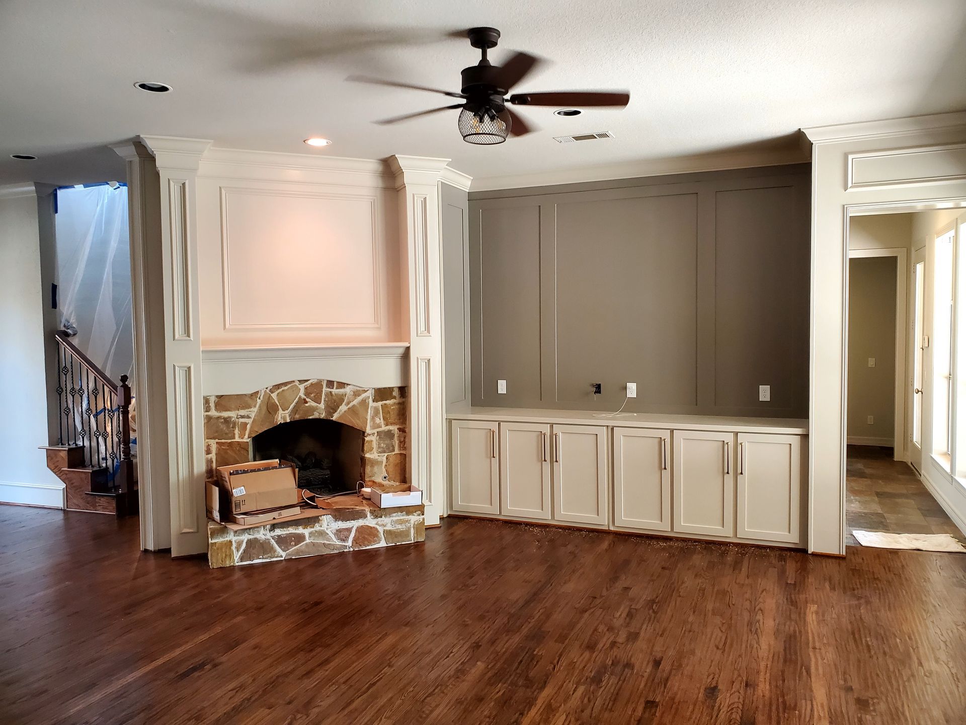 Living room with stone fireplace, built-in cabinets, dark wood floors, and a ceiling fan.