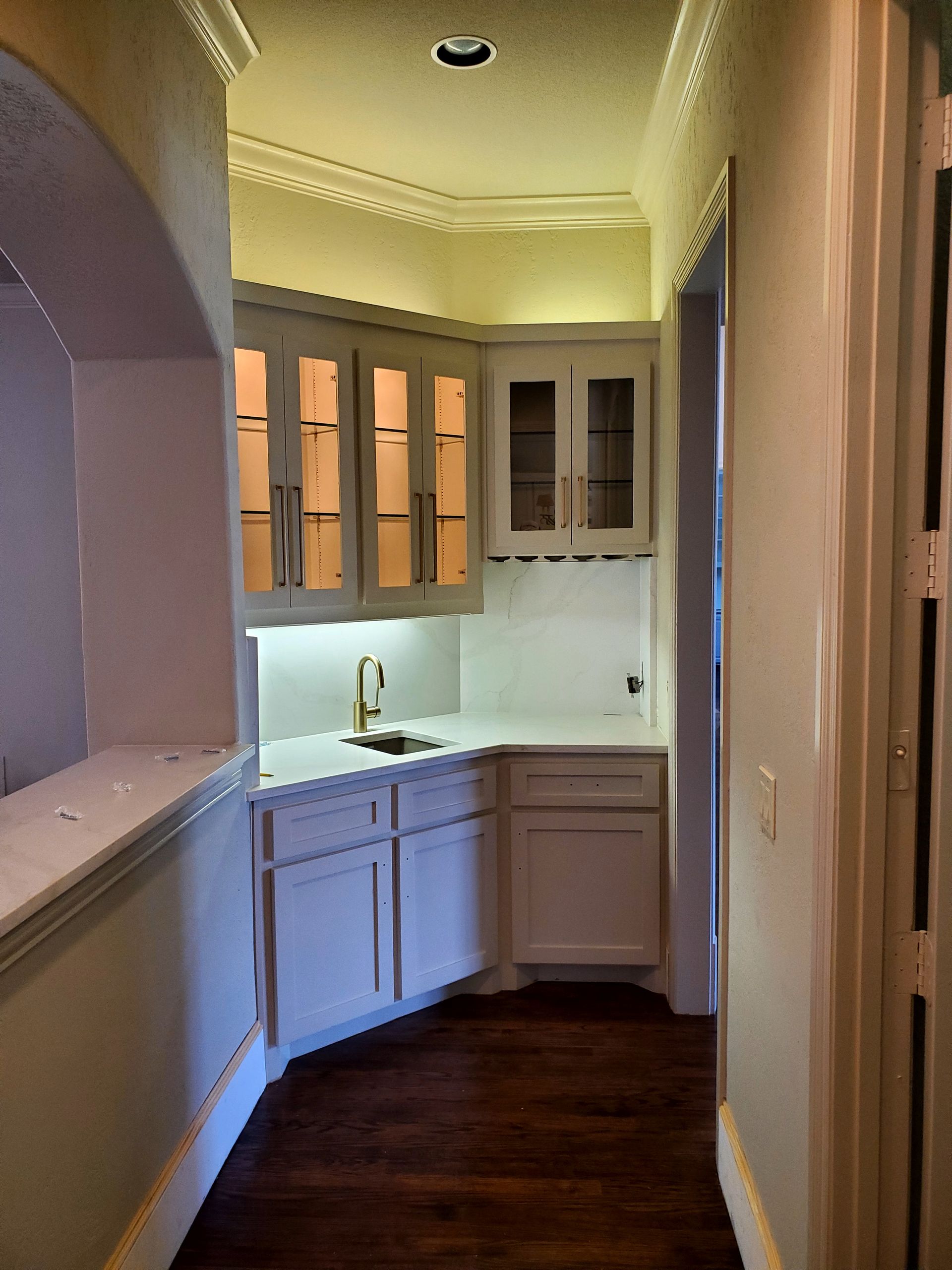 A small white bar area in a hallway with cabinets, a sink, and a wine rack.