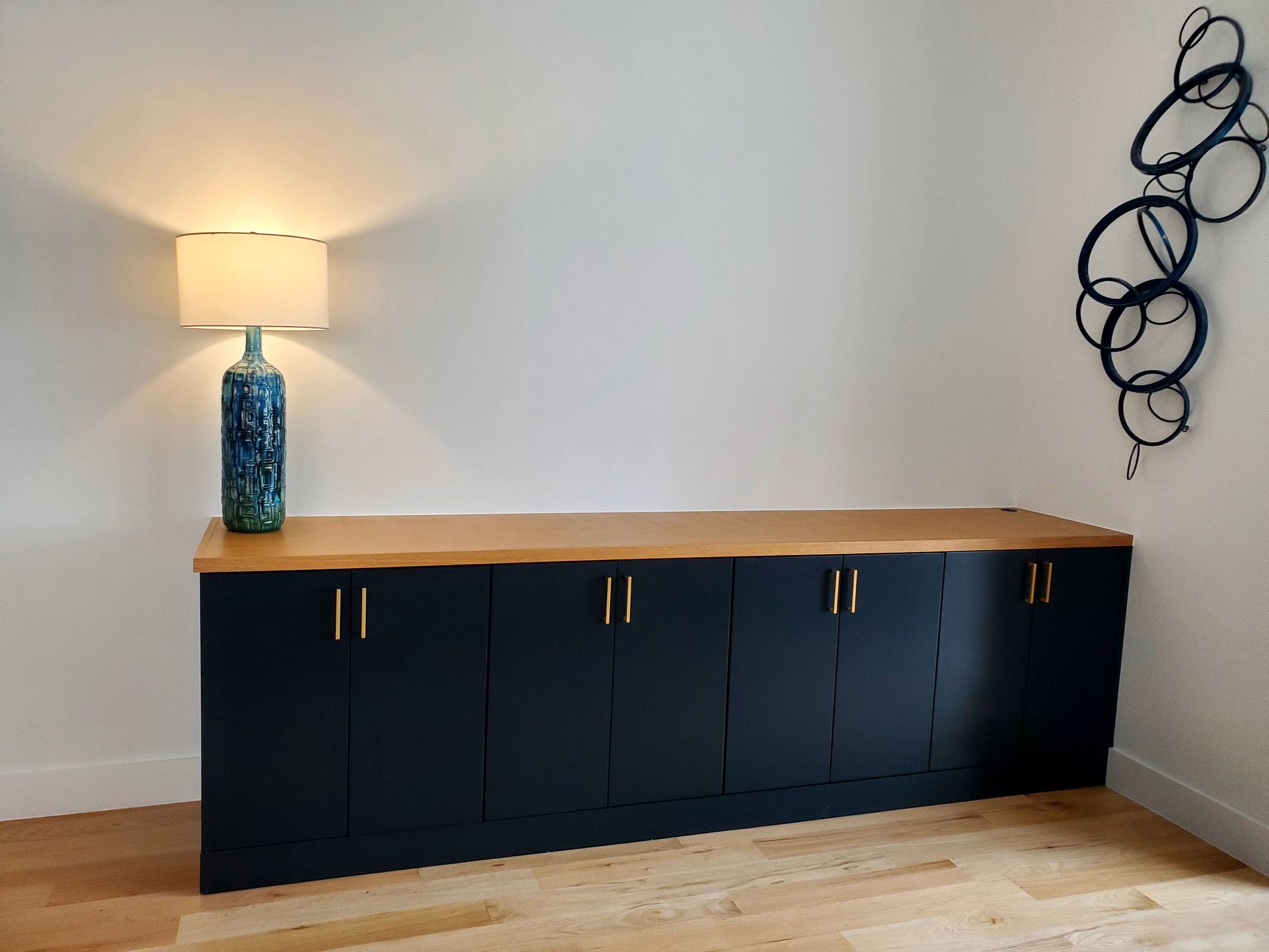 Navy cabinet with wood countertop, gold handles. A lamp and blue art accent the white wall.