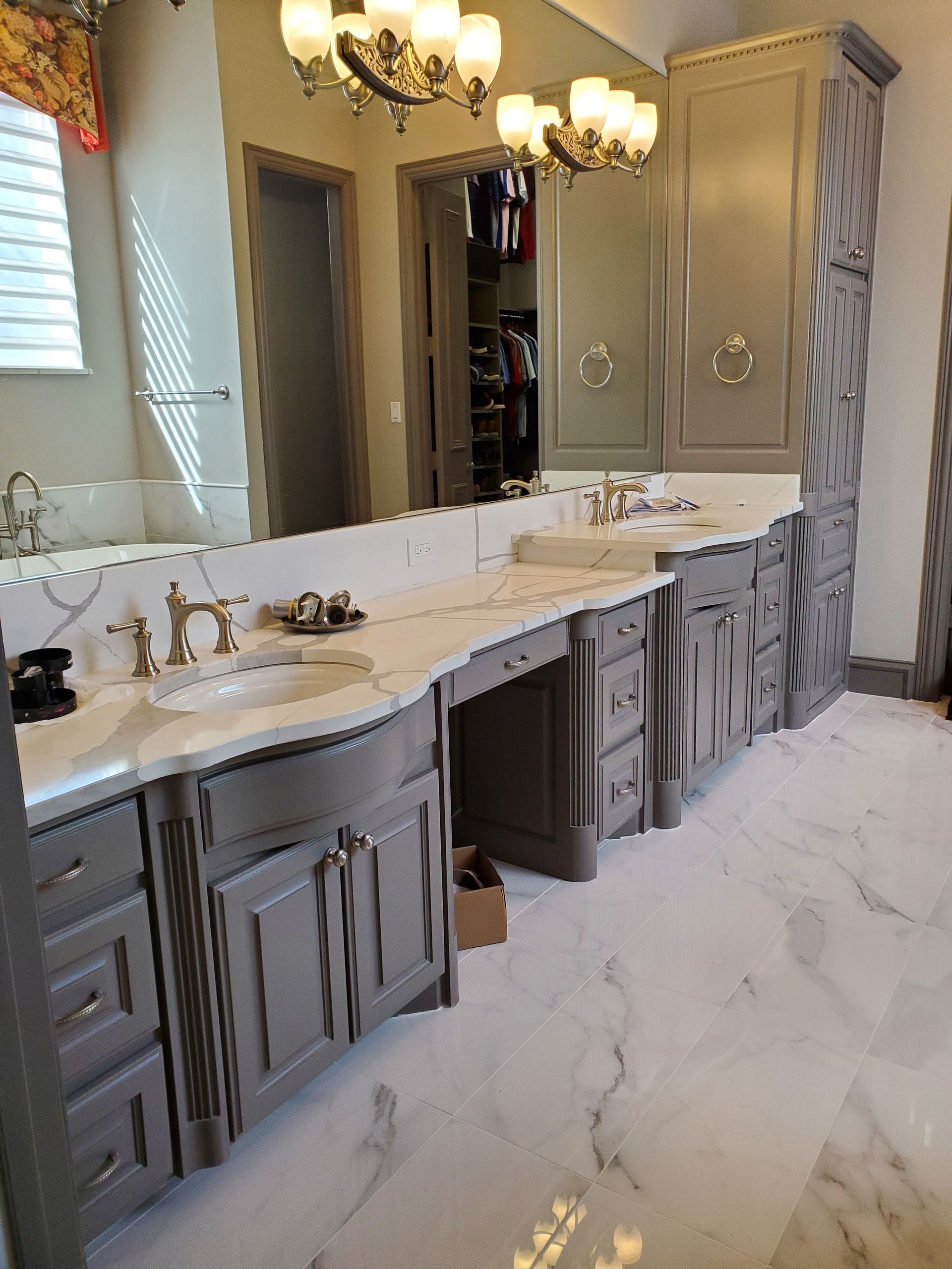 Gray bathroom vanity with marble countertop, two sinks, and tall storage cabinets, in a luxurious bathroom.