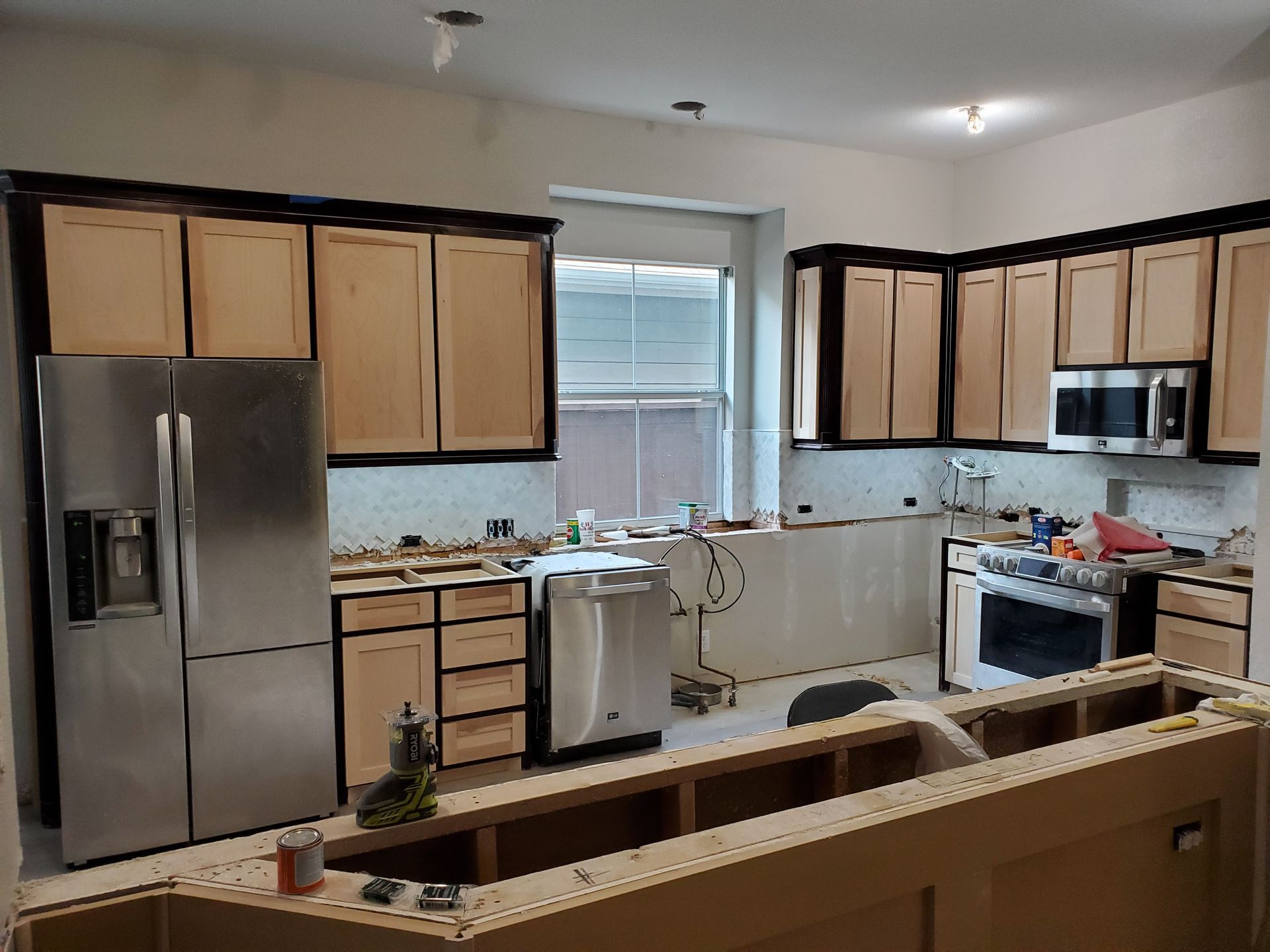 Kitchen undergoing renovation, with stainless steel appliances, unfinished cabinets, and visible construction materials.