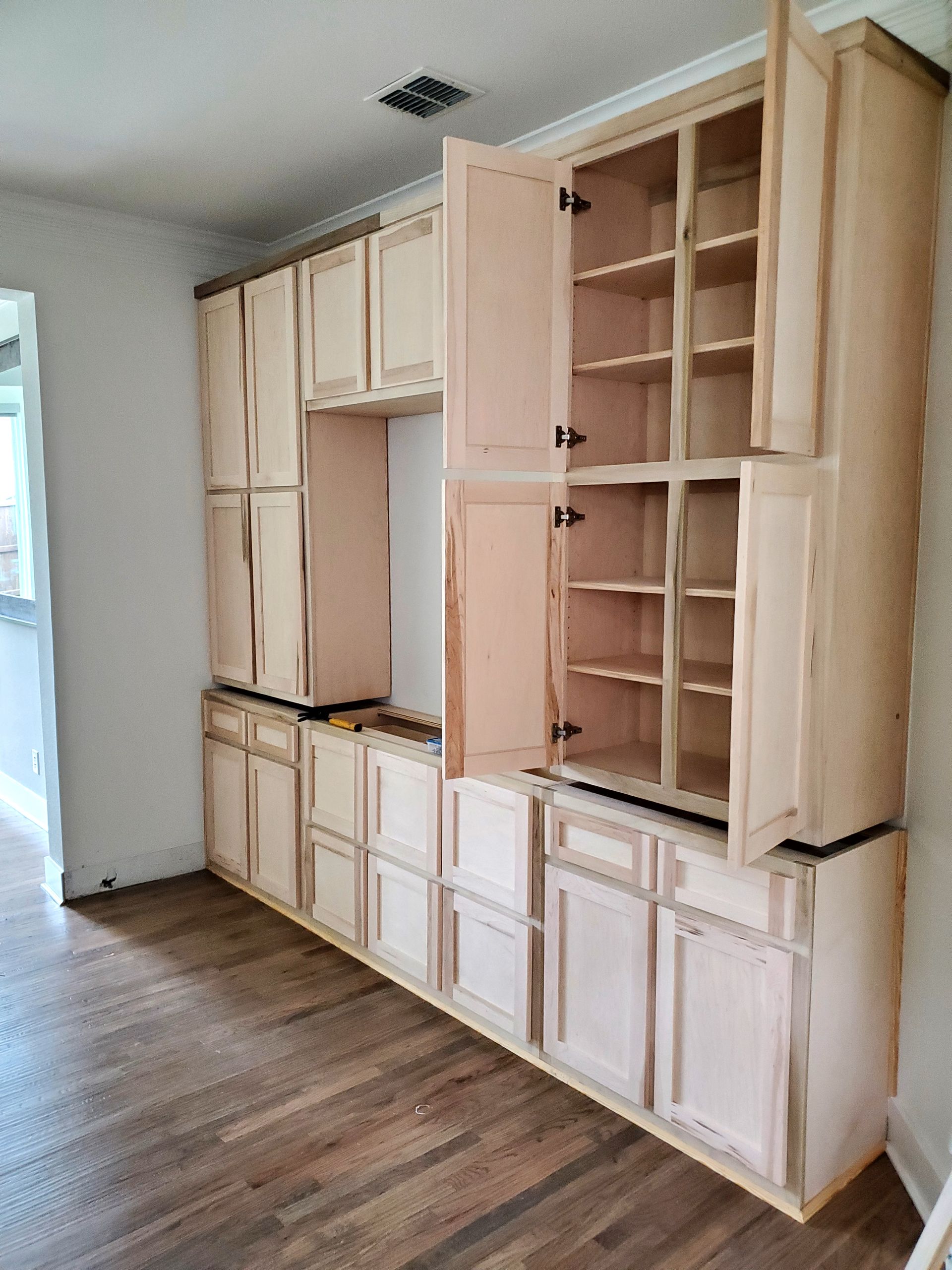 Light wood kitchen cabinets in various sizes with open doors, ready for installation or painting.