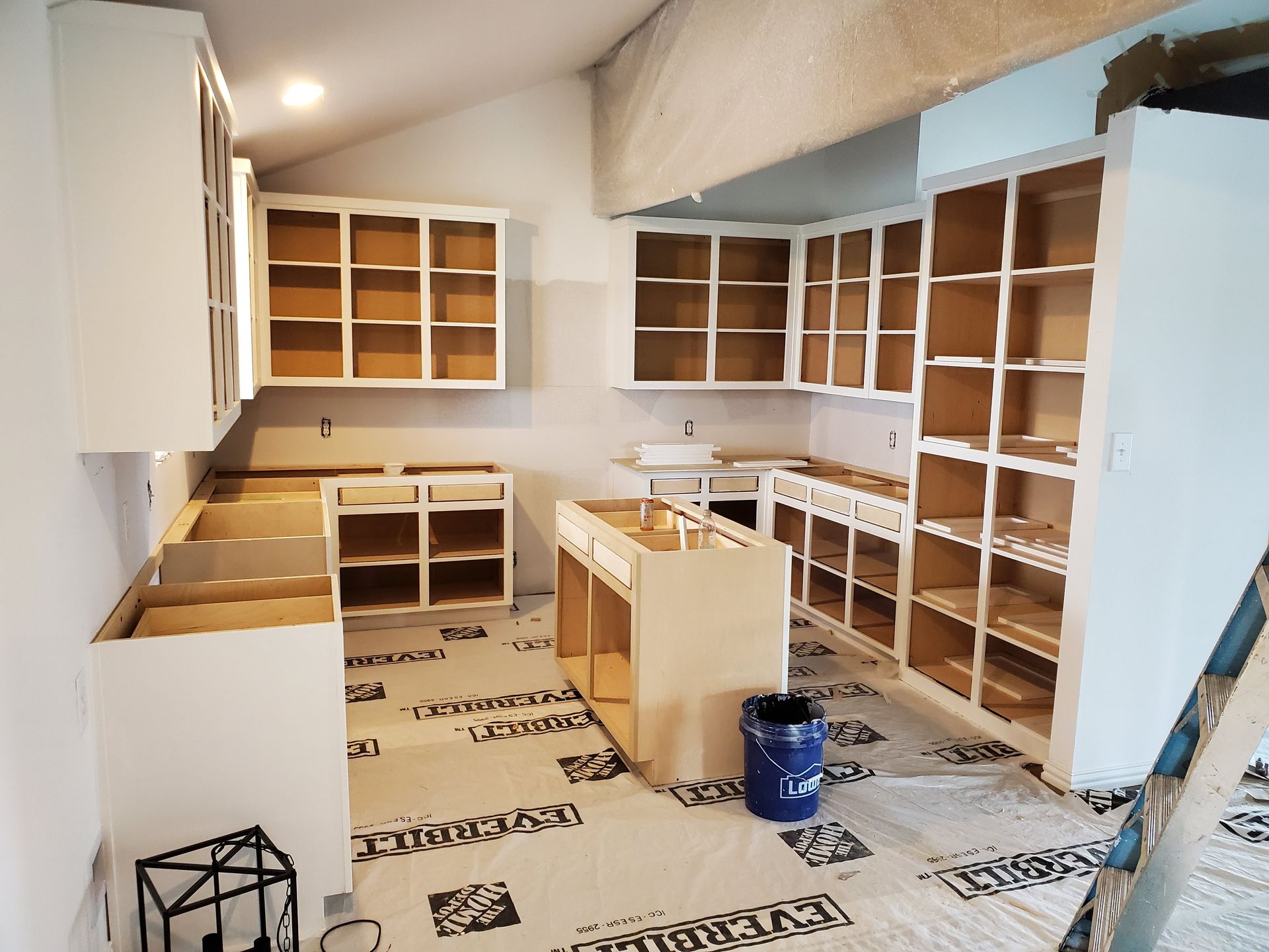 Kitchen under construction, cabinets installed. The unfinished cabinets are white and the interiors are a light wood color. 