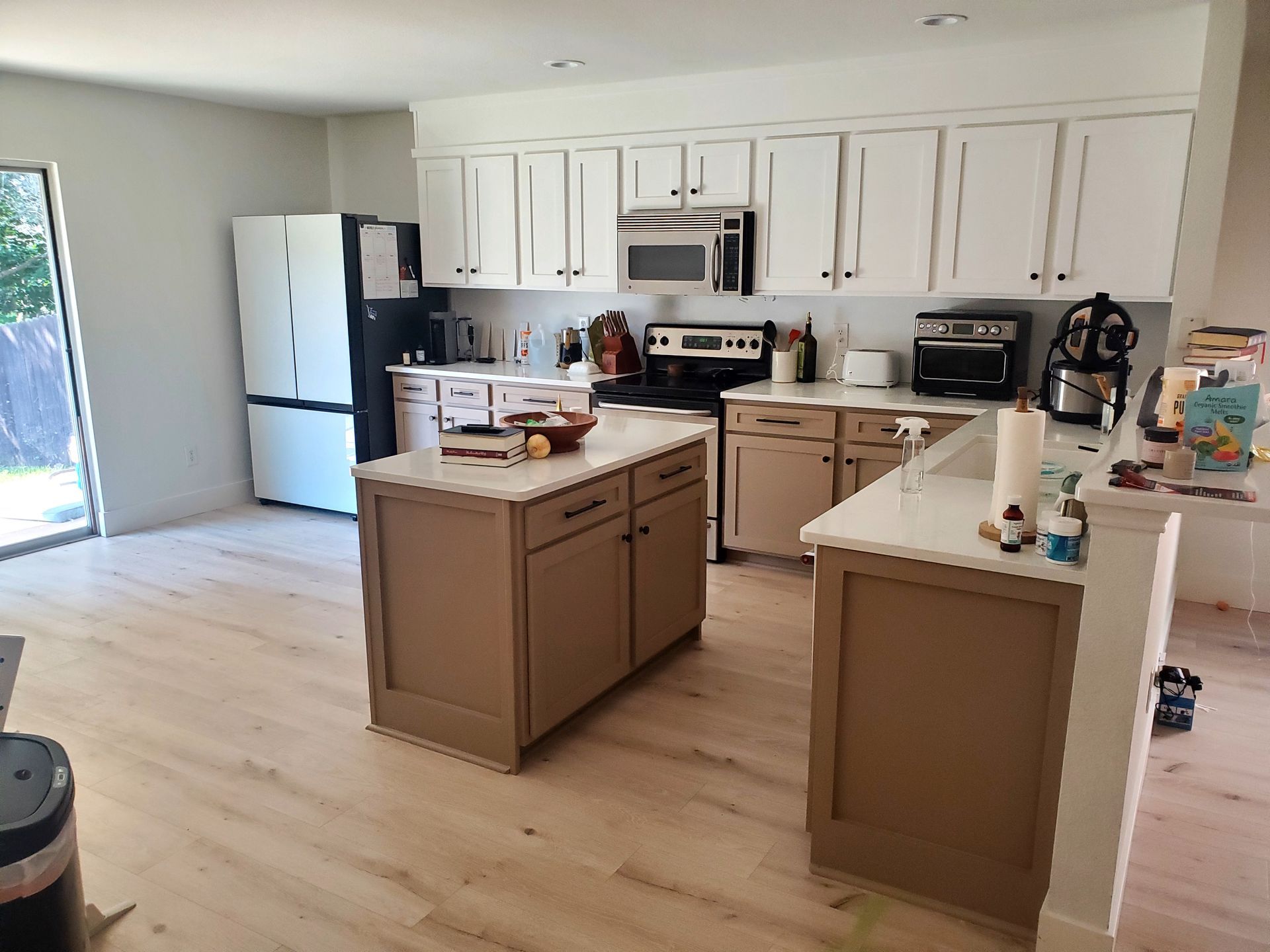 A kitchen with white upper cabinets and brown lower cabinets, a central island, and light wood-look flooring.