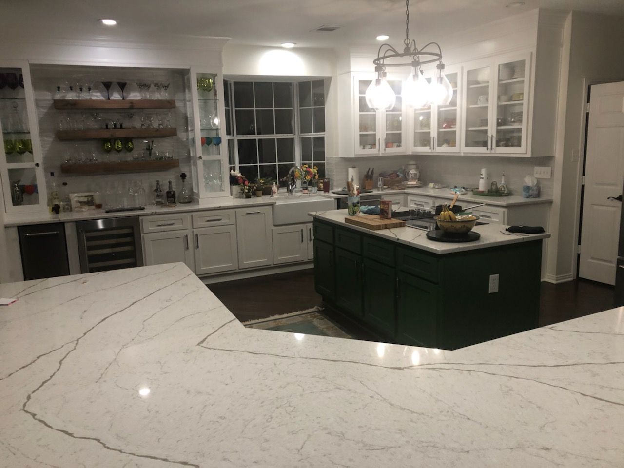 A spacious kitchen with white cabinets, a green island. A built-in bar with wine glasses is on the left.