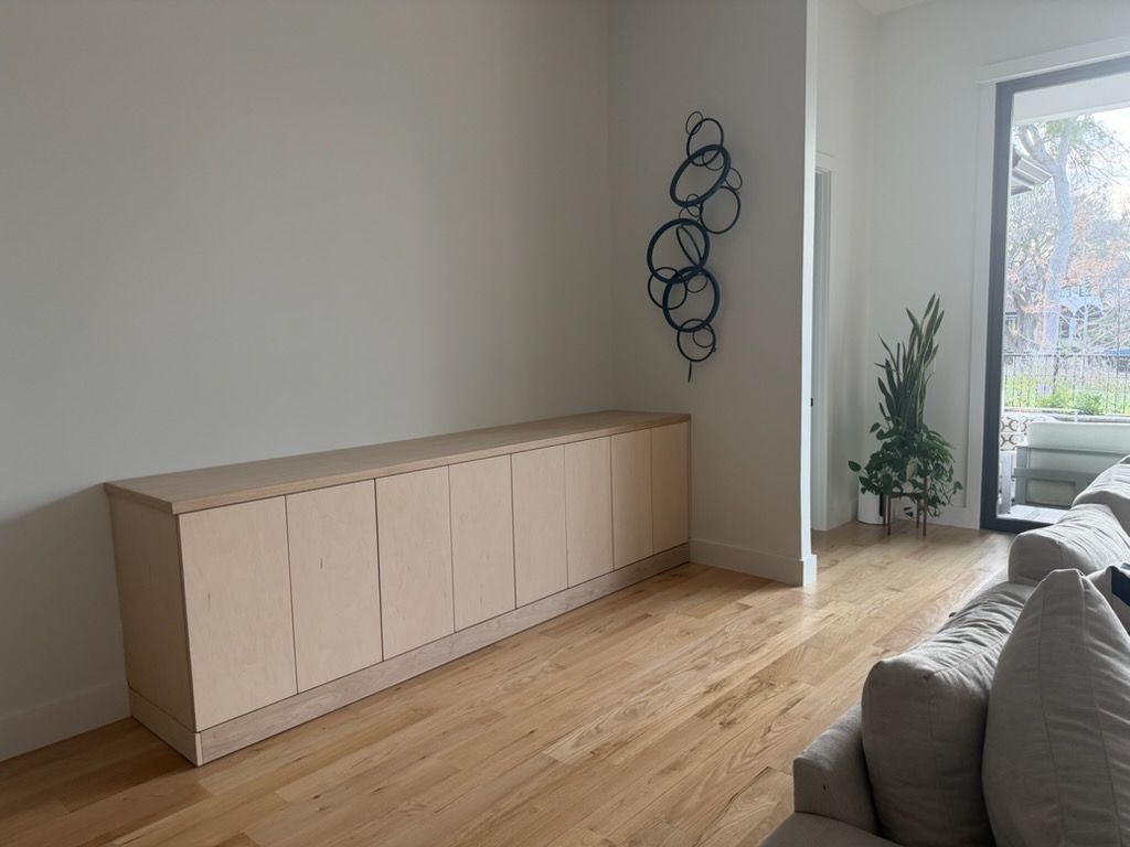 Light wood cabinet against a white wall with metal art. Hardwood floor and a view of a patio.