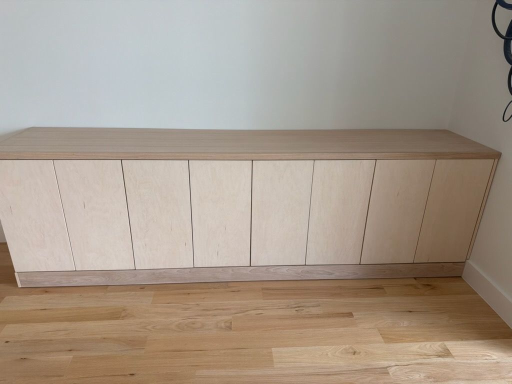 Light wood cabinet with six doors against a white wall and hardwood floor.