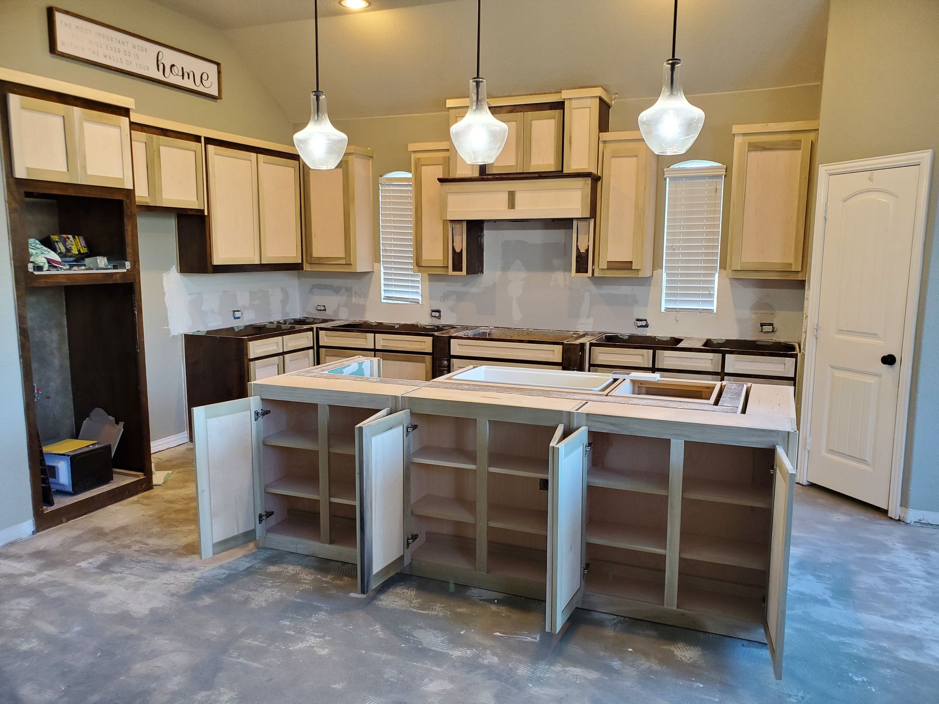 Kitchen under construction with light cabinets, island with open doors, and pendant lights.