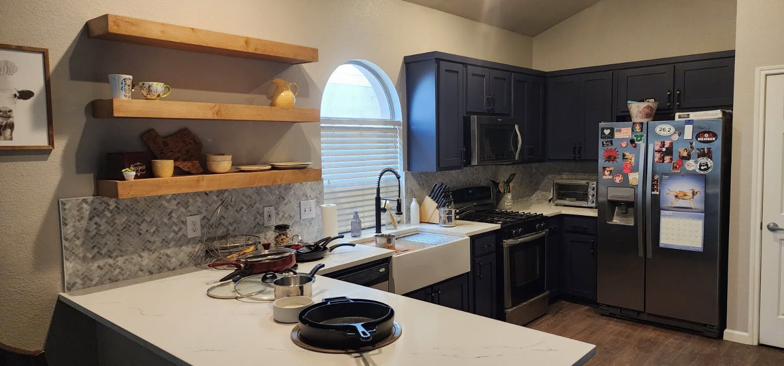 A kitchen with navy cabinets, stainless steel appliances, a white countertop, and wooden shelves.