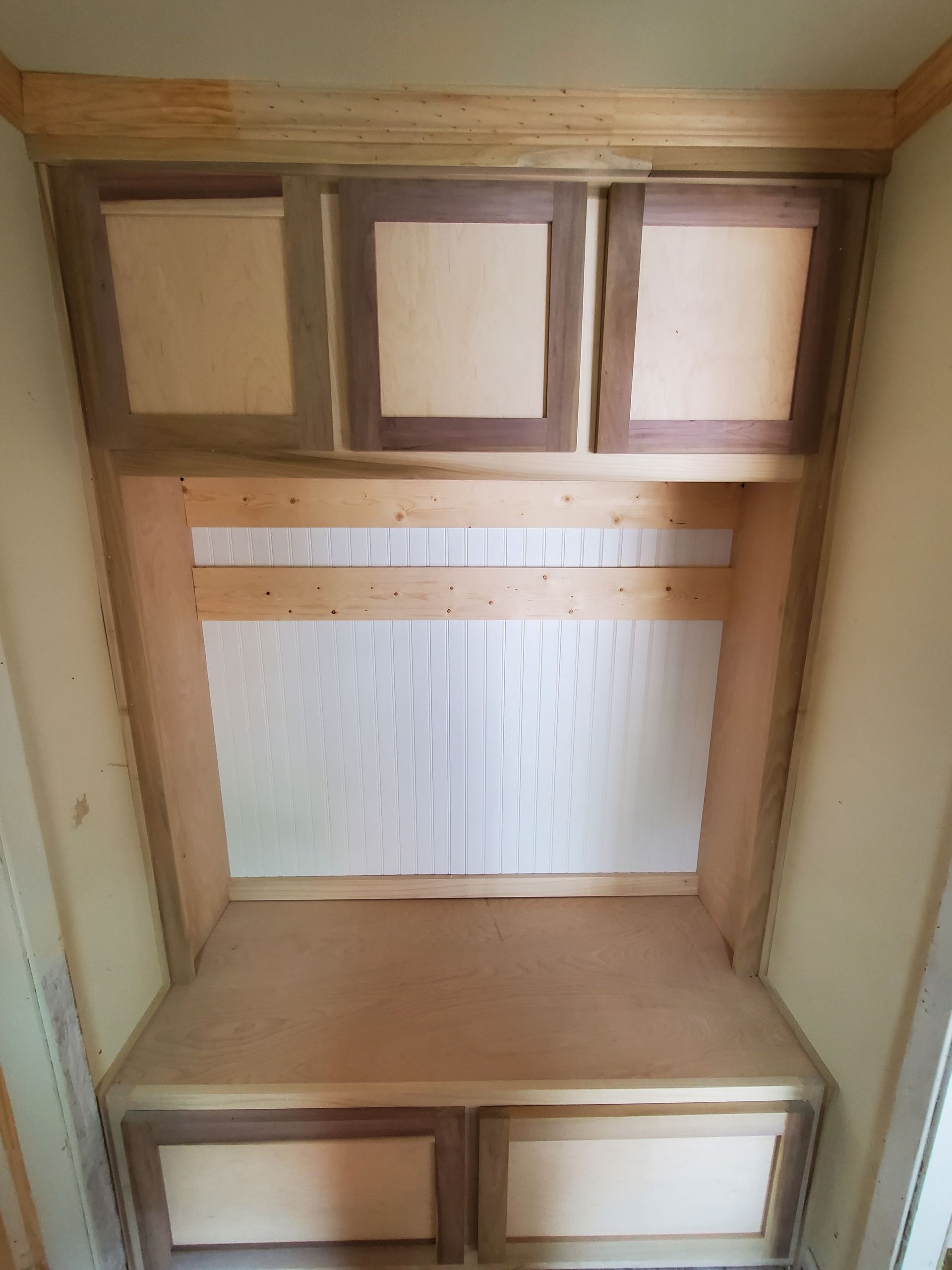 Built-in wooden cabinetry with two lower drawers and three upper cabinets. Light wood with darker trim in a recessed alcove.