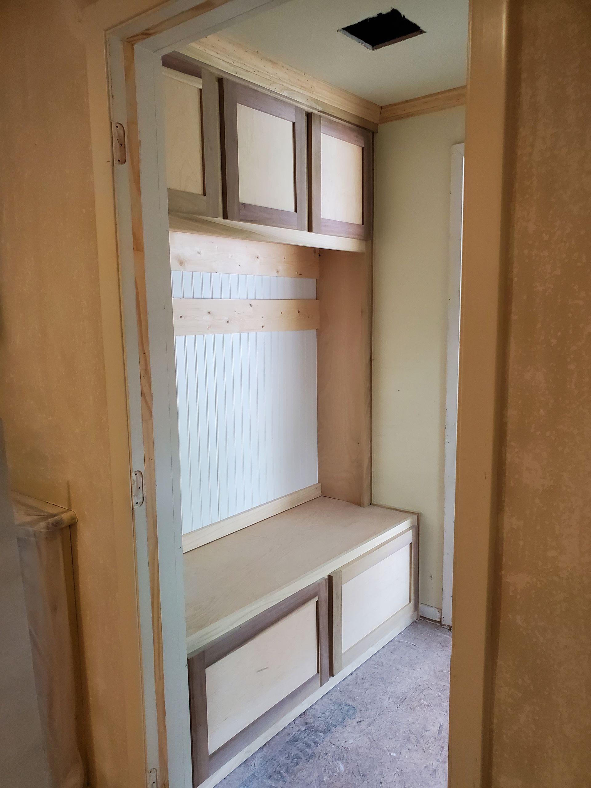 Built-in entryway bench with storage cabinets. Light wood and white accents fill the small space.