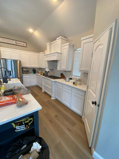 White kitchen with light wood floors, white cabinets, and a blue island. Stainless steel appliances.