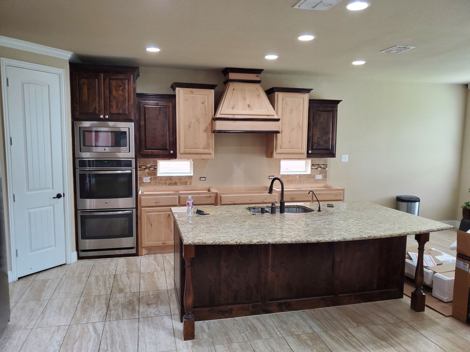 A kitchen with a dark wooden island and cabinets, light countertops and flooring, and stainless steel appliances.
