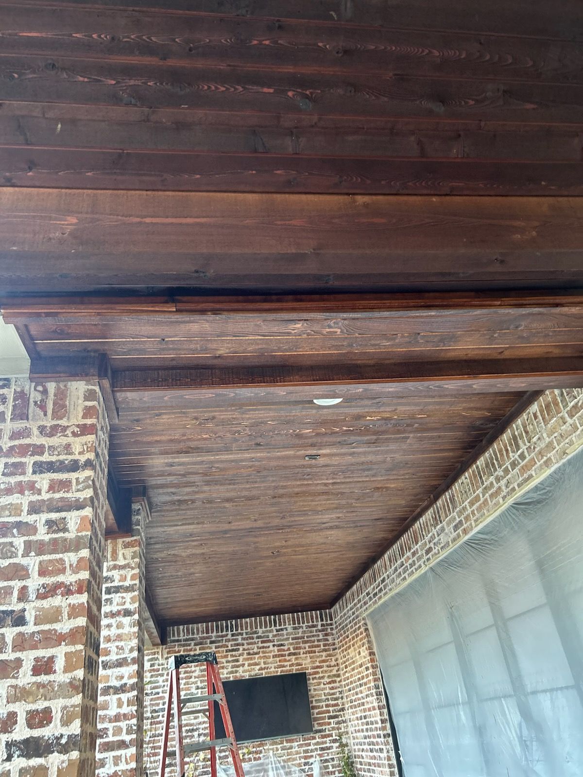 Dark wooden ceiling with brown brick supports. A ladder leans against the wall below the ceiling.