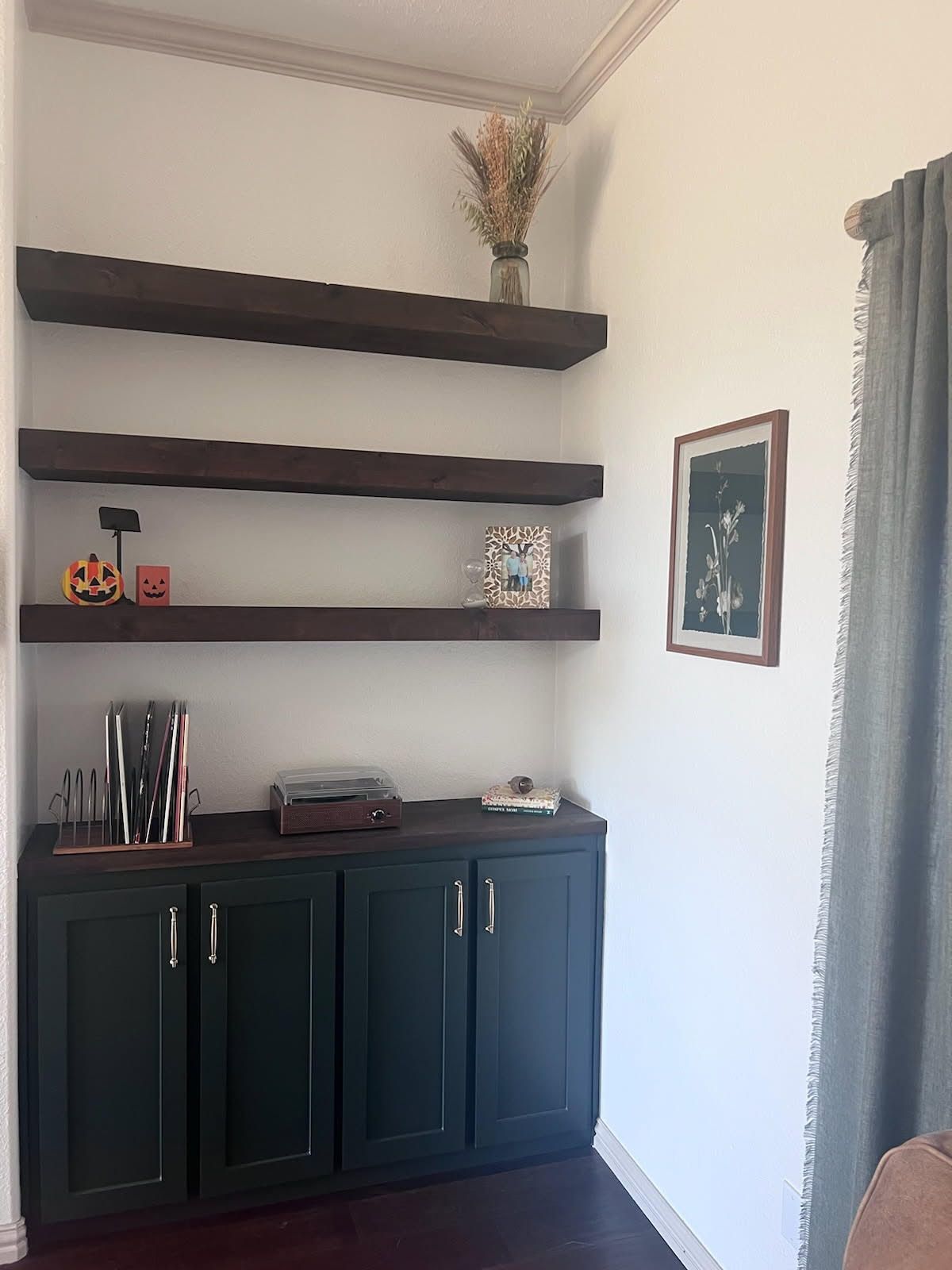 Built-in shelves with dark wood and green cabinets in a corner. Dried flowers and decor on display.