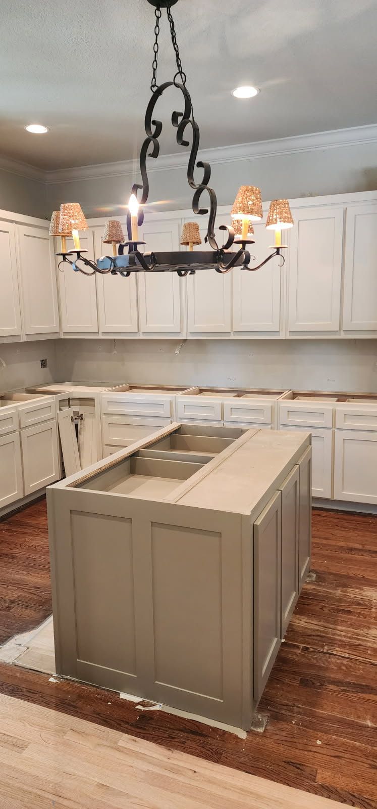 Kitchen with a gray island and light-colored cabinets. A dark chandelier hangs above.